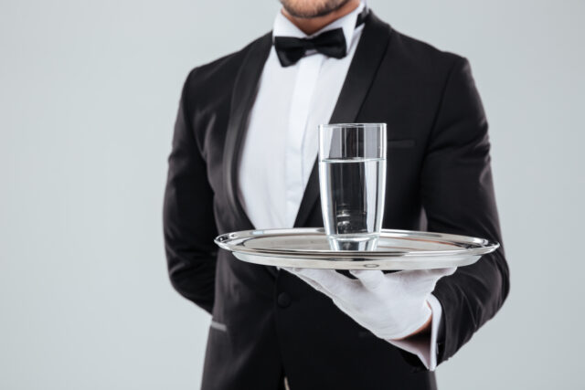 Closeup of butler in tuxedo and gloves holding silver tray with glass of water:Quick and Easy Hacco Recipes, as Enjoyed by Top Models