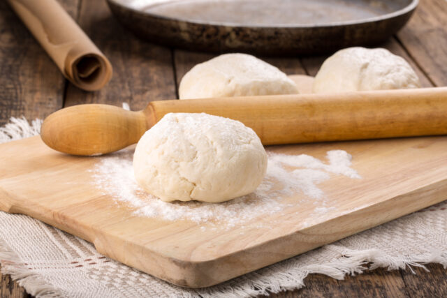 Fresh shortcrust dough pastry and rolling pin on table. Unrolled and unbaked. Ready for baking.