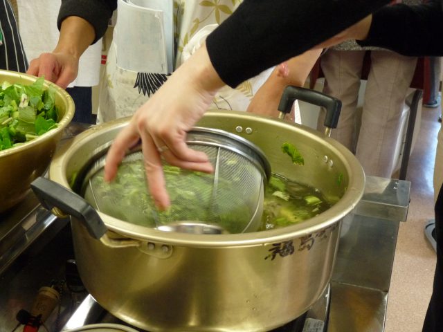 大鍋に65度くらいのお湯を用意し、ザルにいれたすんきの茎を湯通しして、その種の上に入れていきます。